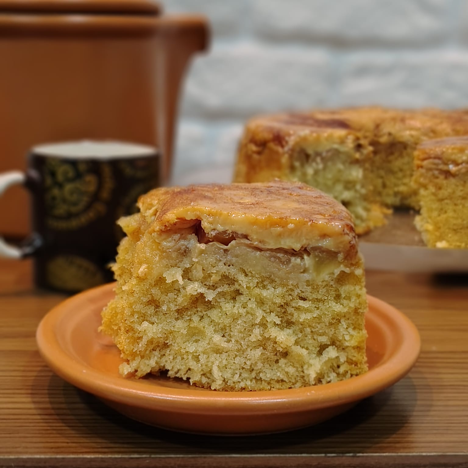 Fatia de bolo de maçã recheado com cobertura cremosa, servida em prato de barro